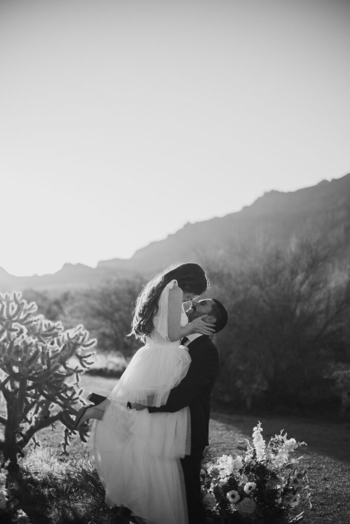 Black and white photo of a bride and groom in the Arizona desert wearing a wedding dress and black suite.