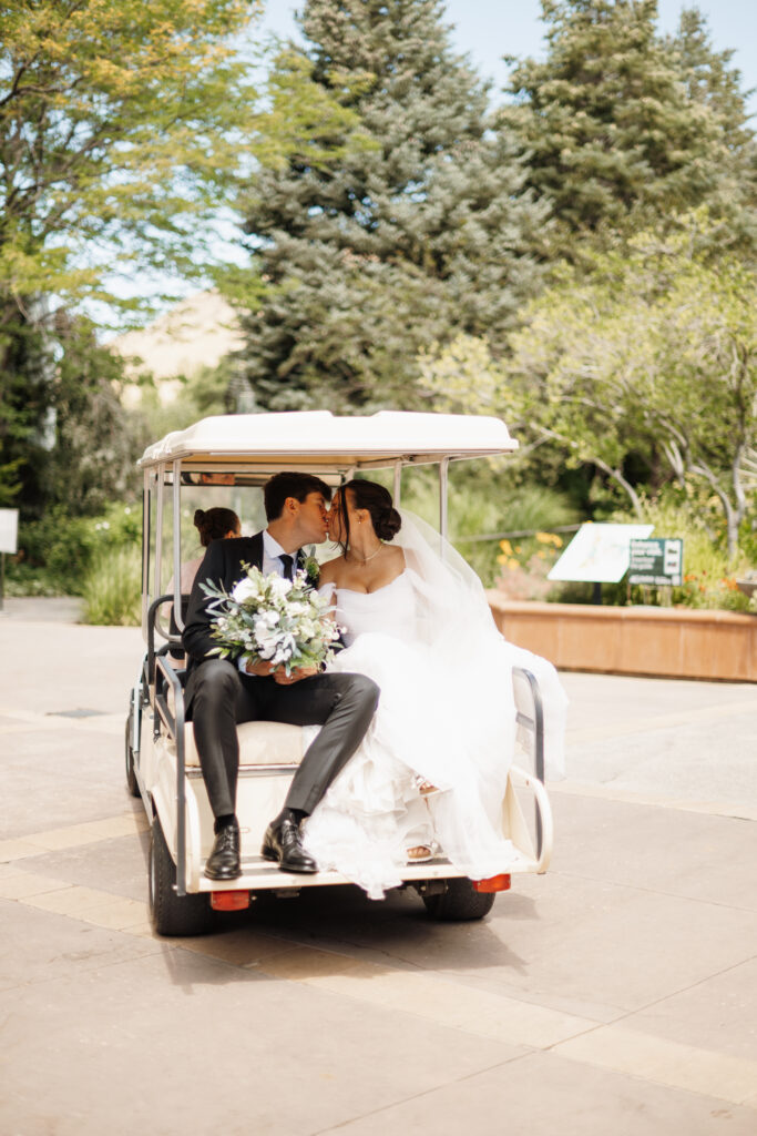Bride and groom on the back of a golf cart in wedding attire