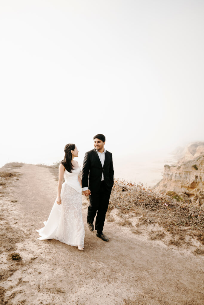 Bride and groom eloping on the California coast in a designer gown and black suit