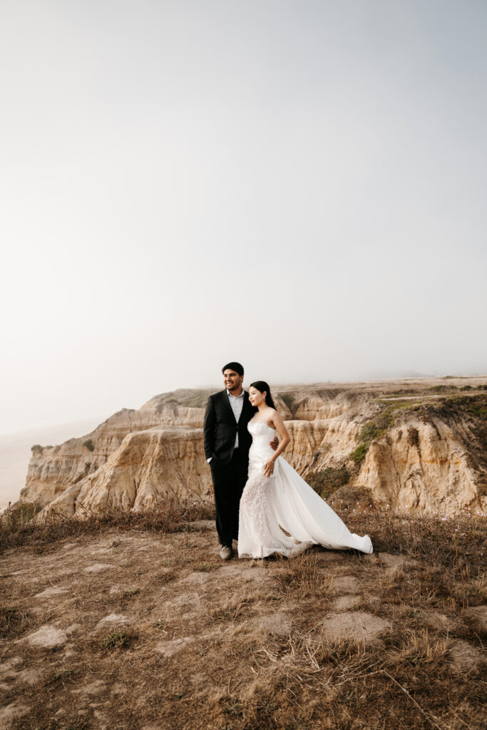 Bride and groom eloping on the California coast in a designer gown and black suit