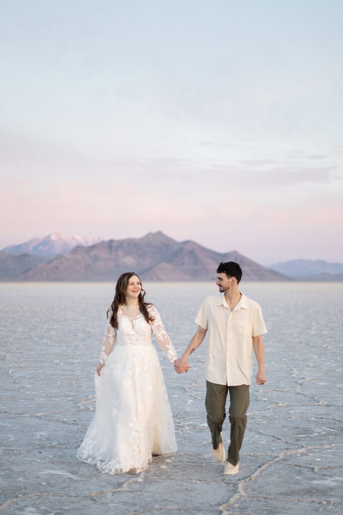 Bride and groom walking across the Bonneville Salt Flats during golden hour bridal session