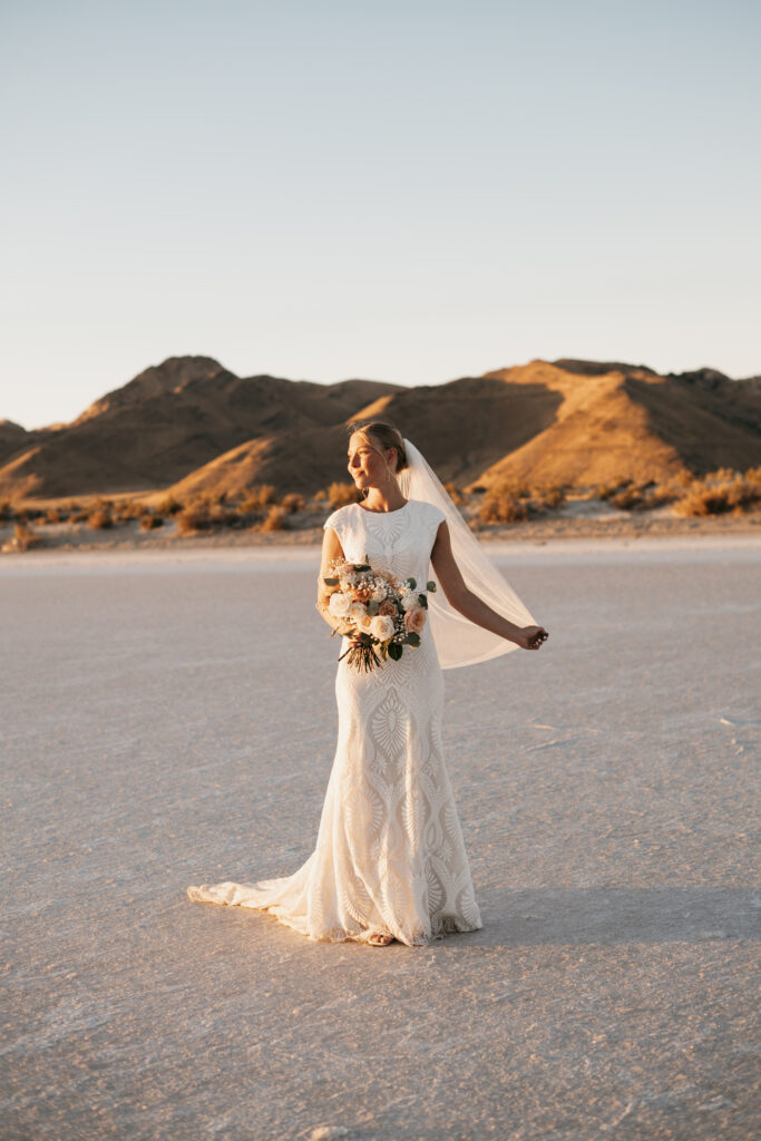 Bride standing alone on Bonneville Salt Flats with long veil blowing in wind